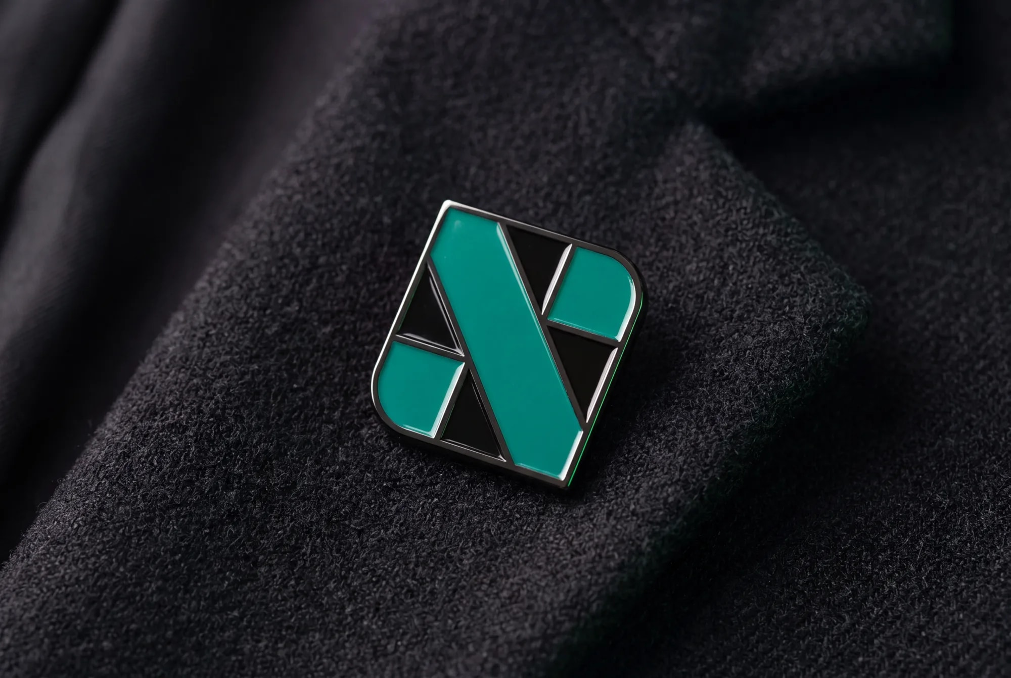 The mark as a hard-enamel pin, signal green on black nickel.